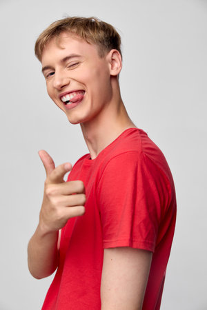 Smiling man in red shirt pointing playfully at the camera, joyful expression, casual studio setup, friendly engagement, lively pose, bright backgroundの写真素材