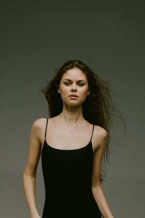 young woman in black dress with flowing hair posing against dark background, confident expression, minimalistic styleの写真素材