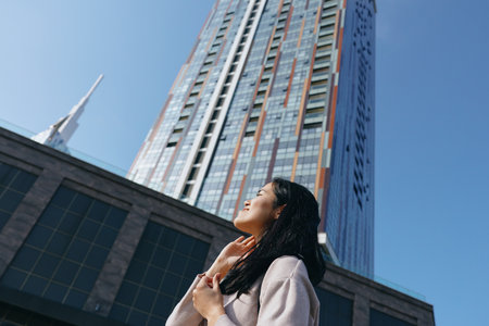 Woman looking up at a towering skyscraper in an urban setting, highlighting ambition, architecture,...