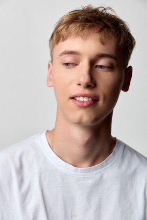 Young man in a white tee gazes aside with a subtle smile, showcasing casual style, everyday comfort, and relaxed mood suitable for lifestyle and fashion scenesの写真素材