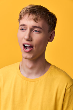 Young man in a yellow shirt sings with open mouth against a bright backdrop, conveying energy and expression for creative projects with impactの写真素材