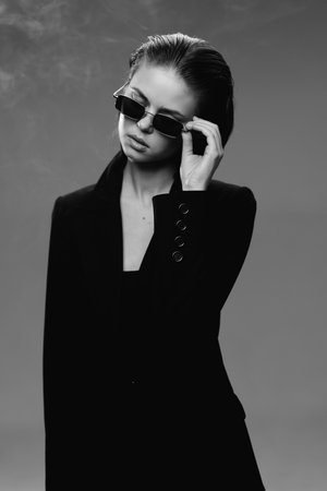 Black and white portrait of stylish woman wearing sunglasses and a blazer, expressing confidence and elegance.の写真素材