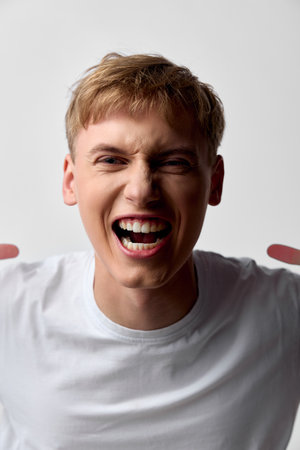 Excited man shouting with a wide smile in a white t-shirt, energetic mood and expressive face, dynamic moment captured, emotion and vigor, casual scene focused on exuberant energyの写真素材