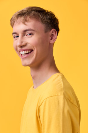 Smiling young man in a yellow shirt stands in a bright studio, cheerful expression and casual fashion captured for lifestyle photography, creating a positive vibe for branding and advertisingの写真素材