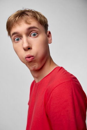 Closeup of a surprised man in a red shirt, capturing a vivid reaction and playful astonishment. Studio lighting highlights facial energy, humor, and a bold, expressive moment.の写真素材