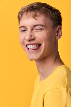 Smiling and wink in a yellow shirt against a solid yellow background, conveying playful energy, casual style, and upbeat mood ideal for lifestyle, fashion, or marketing campaigns.の写真素材