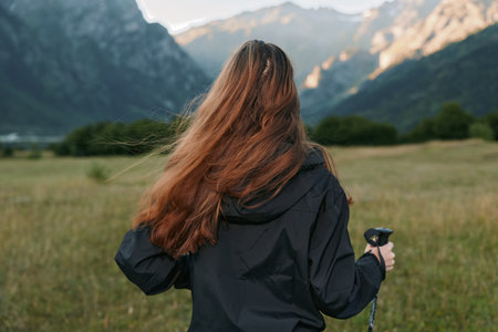 A lone hiker stands in a grassy field, back facing the camera, gazing toward distant mountains under clear skies, enjoying the peaceful outdoor landscape.の写真素材