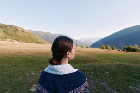 Woman back view looking at mountain valley and meadow landscape, nature travel scene with peaceful...
