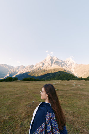 Woman in profile standing in a wide field with mountains in the background, landscape and nature...