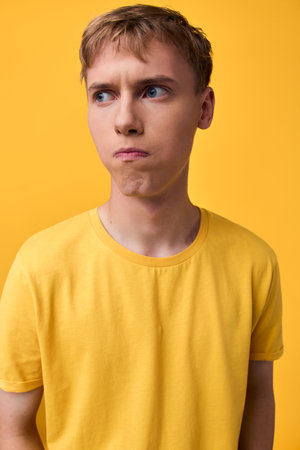 Puzzled expression on a young man wearing a bright yellow shirt against a matching yellow studio...