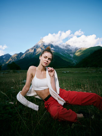 Active outdoor scene featuring a woman in a white sports top and red pants resting on grass with a...