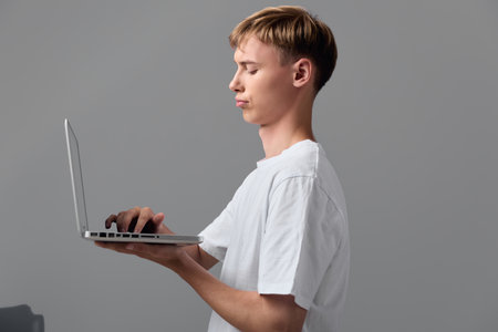 Man with a laptop in hand, side view profile, focused on screen for remote work, learning and...