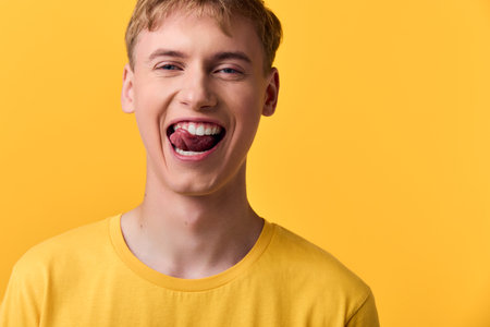 Playful, yellow clad youth with a tongue out smile in a bright studio, conveying bold fashion and energetic mood, ideal for lifestyle, humor, and youthful expression in creative campaignsの写真素材