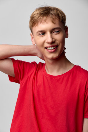 Smiling man in a red tshirt poses casually with a hand behind the neck in a bright studio, conveying relaxed lifestyle fashion and everyday confidence for lifestyle or fitness projectsの写真素材