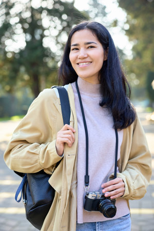 Casual outdoors photographer carrying backpack and camera, smiling in park, ready to capture candid...
