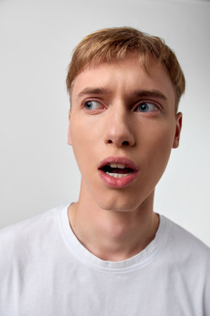 Surprised man face expression close up in a white t shirt, wide eyes and open mouth convey...