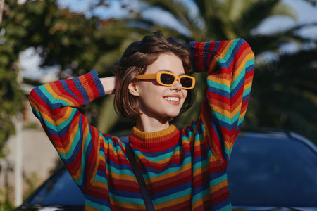 Woman smile sweater sunglasses rainbow portrait of a young woman outdoors, colorful striped sweater, short hair, casual fashion, sunny day, relaxed joyful expression near car.の写真素材