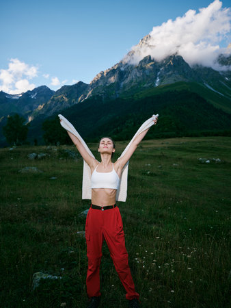 Outdoor scene with a athletic woman in a white crop top and red pants, arms raised, standing in a...
