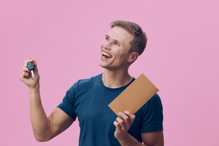smiling caucasian man hold car key and envelope look up excited casual clothing pink background...