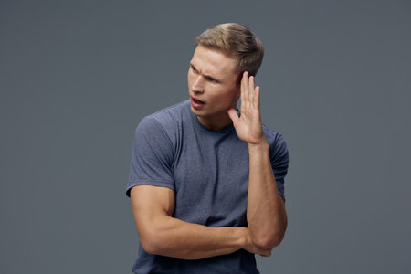 confused young caucasian man wear blue shirt listen hand near ear isolated on grey background studio...