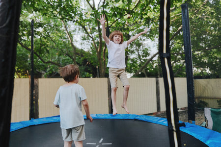 Jumping boy on a trampoline, cheerful atmosphere, sunlight filtering through trees, outdoor fun, playful moment, vibrant colors.の写真素材