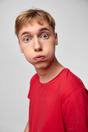 Surprised young man in a red shirt with wide eyes and puckered lips, studio setup, captured for humorous reaction and expressive stock imagery.の写真素材