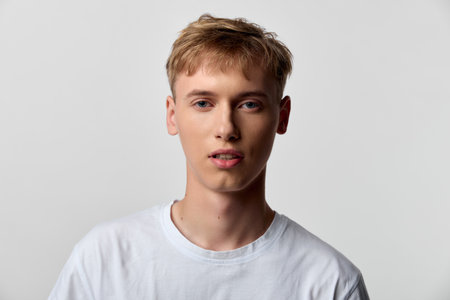 Young man wearing a white tee against a neutral backdrop, close up facial expression, casual studio...
