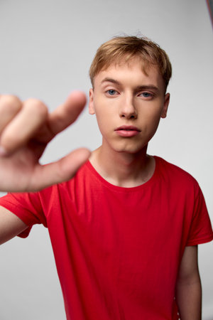 Close up of a young man in a red shirt reaching toward the camera, hand in foreground, focused gaze...