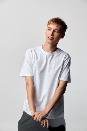 Casual man wearing a white t shirt modeling in studio with a relaxed pose, clean background, and...