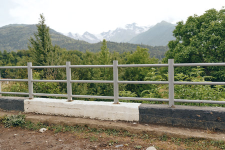 Railing and low barrier overlook a scenic mountainous landscape with trees and distant peaks, creating a peaceful outdoor scene filled with natural calm and opennessの写真素材