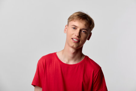 Young man wearing a red t shirt in a studio setting with a relaxed expression, showcasing casual fashion and contemporary style for lifestyle and stock photography.の写真素材