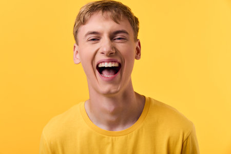 Laughing man wearing a yellow shirt against a bright yellow backdrop, expressing joy and cheer. Studio shot focusing on bold color, lively mood, and positive energy.の写真素材