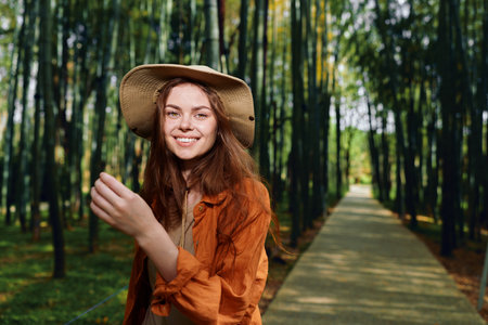 Woman smile hat forest path walkway nature portrait of a happy young female outdoors on a wooden boardwalk, candid travel lifestyle photo with sunlight and relaxed expressionの写真素材
