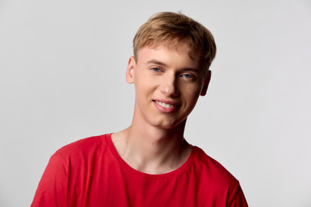 Smiling man wearing a red t-shirt in a bright studio with soft lighting and a clean grey background, casual and approachable vibe, suitable for lifestyle, fashion, or corporate culture concepts.の写真素材