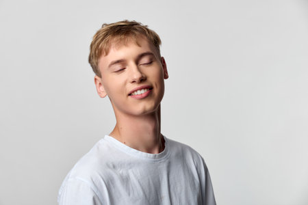 Young, relaxed man with a gentle smile wearing a white shirt in a minimal studio setting, exuding calm confidence and serene mood through soft lighting and clean backgroundの写真素材