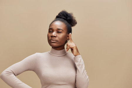 Thoughtful young woman in a beige top reflecting on ideas, with a contemplative expression and a...
