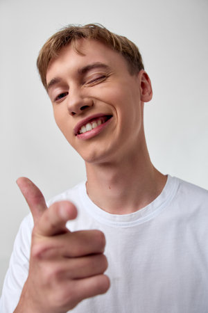 Pointing, smiling man in a casual white t-shirt delivers a confident message, close up shot for...