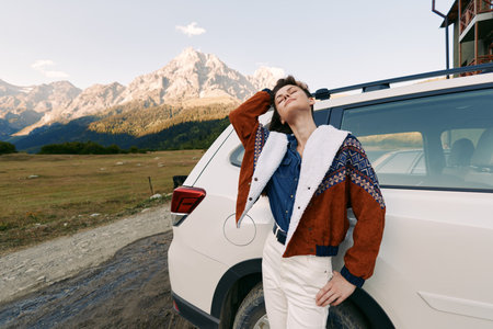 Woman, car, mountains, headphones, travel, roadtrip, nature, relaxation: Young woman leans against...