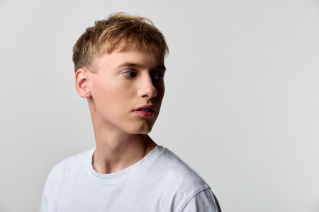 Man in a white t shirt posed against a light backdrop, turned to the side with a contemplative look, minimal studio style and clean casual fashionの写真素材