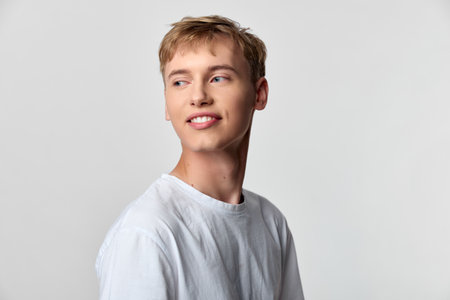 Smiling man in a white t shirt looks to the side in a clean studio setting, conveying ease, confidence, and approachable charm for lifestyle or fashion concepts.の写真素材