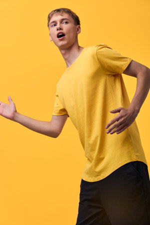 Man in a yellow shirt strikes a dynamic pose with open arms and surprised expression against a...