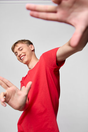 Dynamic shot of a smiling youth reaching toward the camera in a bright red shirt, conveying energy,...