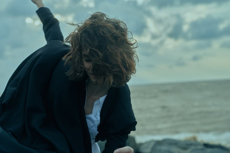 Beach scene with wind, motion, and a businesswoman in blazer and white shirt, outdoors by the sea,...