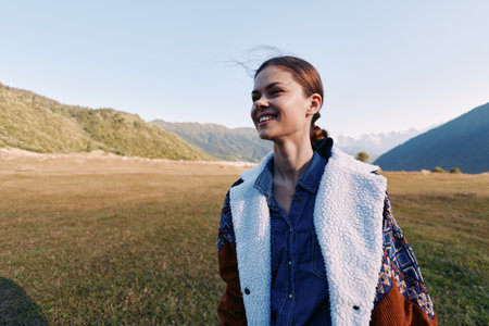 Woman smile portrait in a jacket in a meadow with mountains outdoors, enjoying travel and nature....
