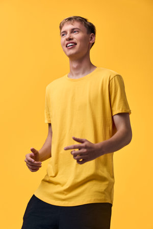 Smiling man in a yellow t shirt stands in a vibrant studio with a casual pose, warm lighting, and cheerful energy for upbeat fashion and lifestyle contentの写真素材