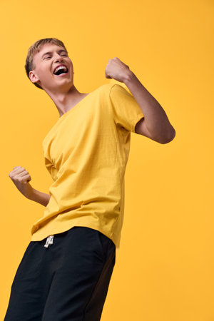 Joyful celebration of energy and happiness, a man in a yellow shirt raises his fists in triumph against a bright backdrop, vibrant pose, dynamic movement and exuberant moodの写真素材