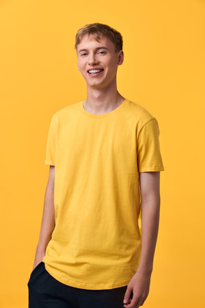 Smiling man in a yellow t shirt stands against a matching yellow backdrop, casual fashion, relaxed pose, studio shot, vibrant color harmony and confident moodの写真素材