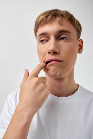 Thinking contemplative man with finger on lip, wearing a white shirt, conveying curiosity, hesitation and reflective mood in a simple studio settingの写真素材