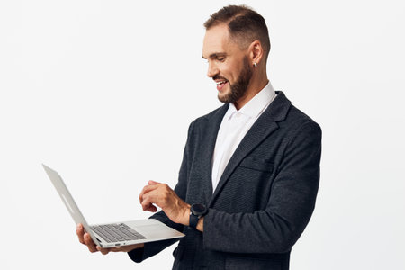 Businessman in a dark blazer works on a laptop, focused and confident against a clean colored...