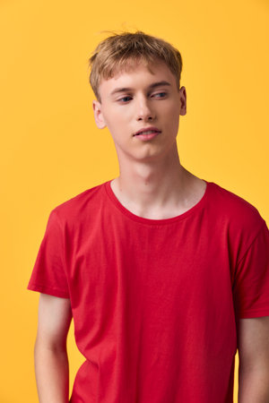 Young man in red t shirt posed casually against a bright yellow background, studio shot for fashion and lifestyle stock with a clean composition and contemporary vibeの写真素材